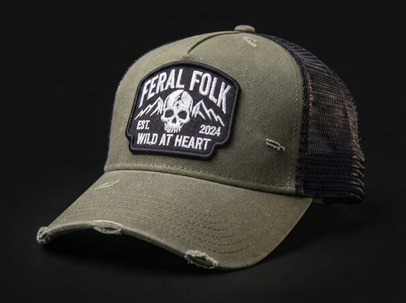 An olive green distressed trucker hat with a black mesh back and a prominent black 'Feral Folk' patch on the front, set against a solid black background.
