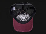 A distressed snapback cap shown from the back, featuring a black mesh back with a white graphic of a skull and roses, and a faded burgundy fabric brim.