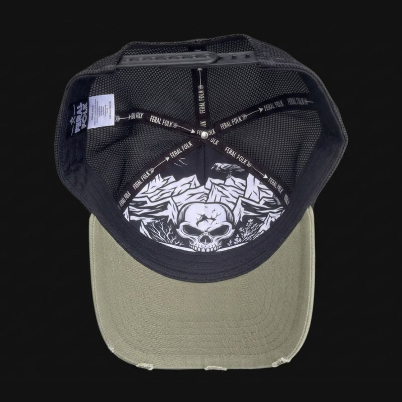 A structured snapback trucker cap shown from the back, featuring a black mesh back with a large white graphic of a skull and mountain peaks, and a distressed olive green brim.
