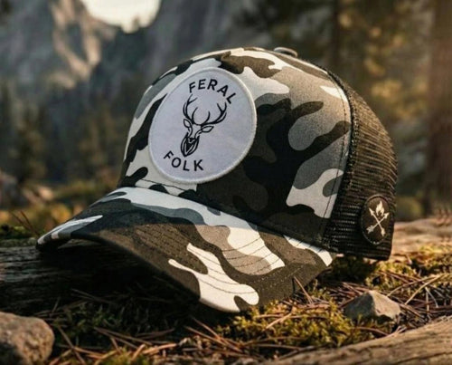 Camouflage trucker hat with 'Feral Folk' logo on a natural background