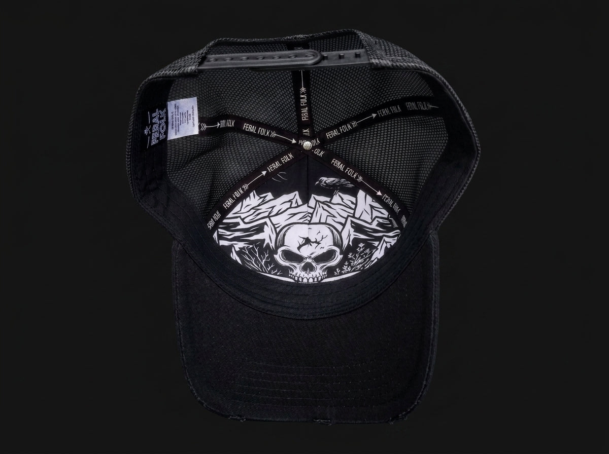 Black trucker-style cap shown from the back, featuring a black mesh back, black adjustable strap with white text, and a white graphic print of a skull and roses on the back panel.