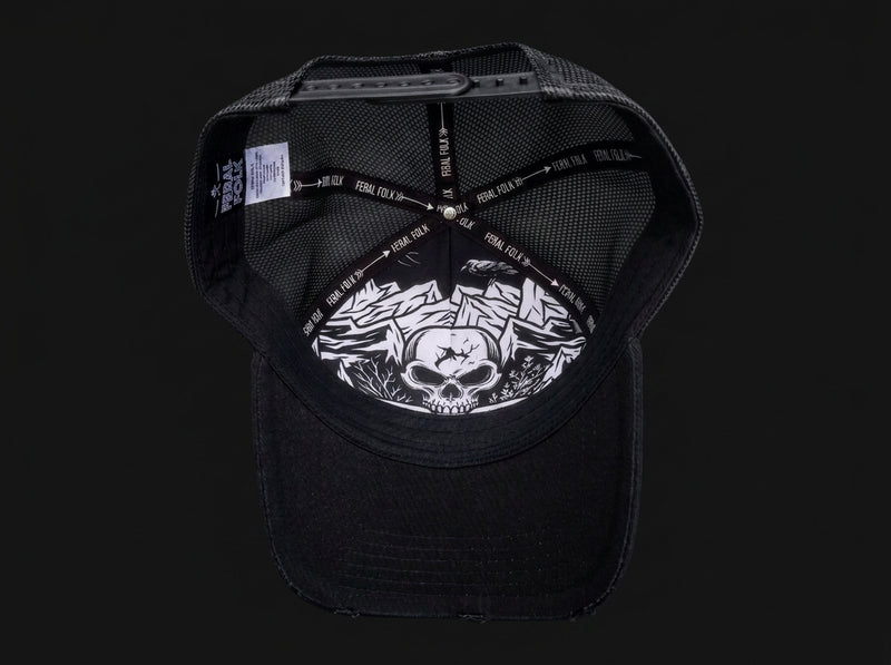 Black trucker-style cap shown from the back, featuring a black mesh back, black adjustable strap with white text, and a white graphic print of a skull and roses on the back panel.